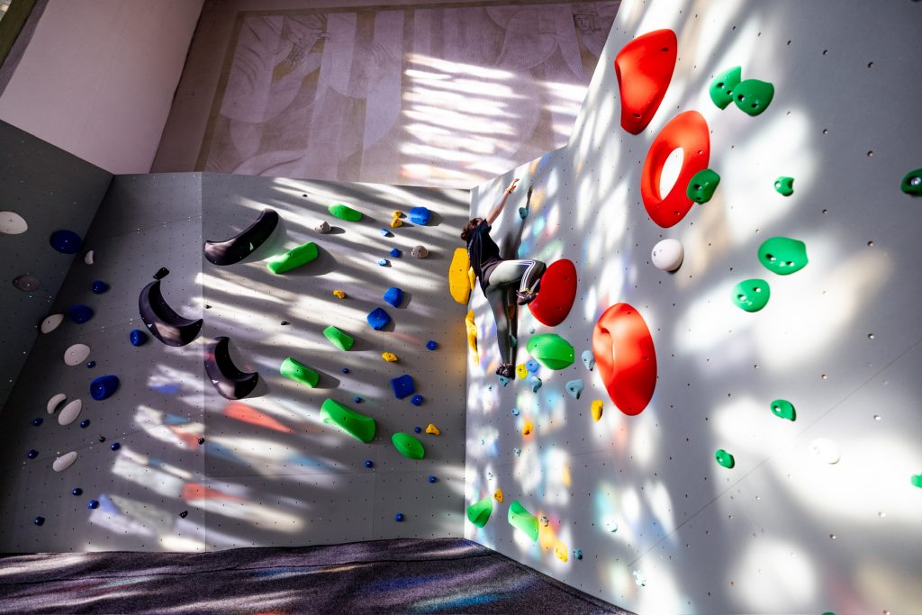 Person beim Bouldern an einer Kletterwand in der Boulder Church Bad Orb, beleuchtet durch farbiges Licht aus Kirchenfenstern.